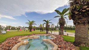 Un jacuzzi rodeado de rocas y palmeras en una zona ajardinada.