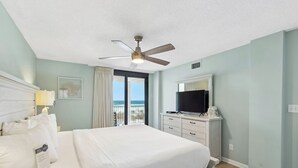 A hotel room with a bed, a ceiling fan, a television, and a view of the ocean.