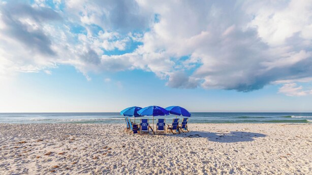 A beach with three blue umbrellas and beach chairs.