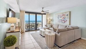 A spacious living room with a large sofa, a coffee table, and a balcony with a view of the ocean.