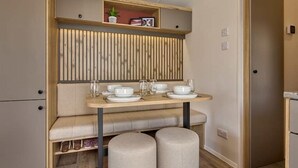 A compact kitchenette with a built-in stove, a small seating area, and a shelf with kitchen essentials.