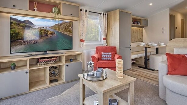A compact living space with a flat-screen TV, a red armchair, a small table with a tray, and a sofa.