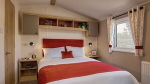 A bedroom with a red headboard, a bed with white and red bedding, a bedside table with a lamp, and a window with curtains.