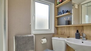 A bathroom with a toilet, sink, towel rack, and a shelf with toiletries.