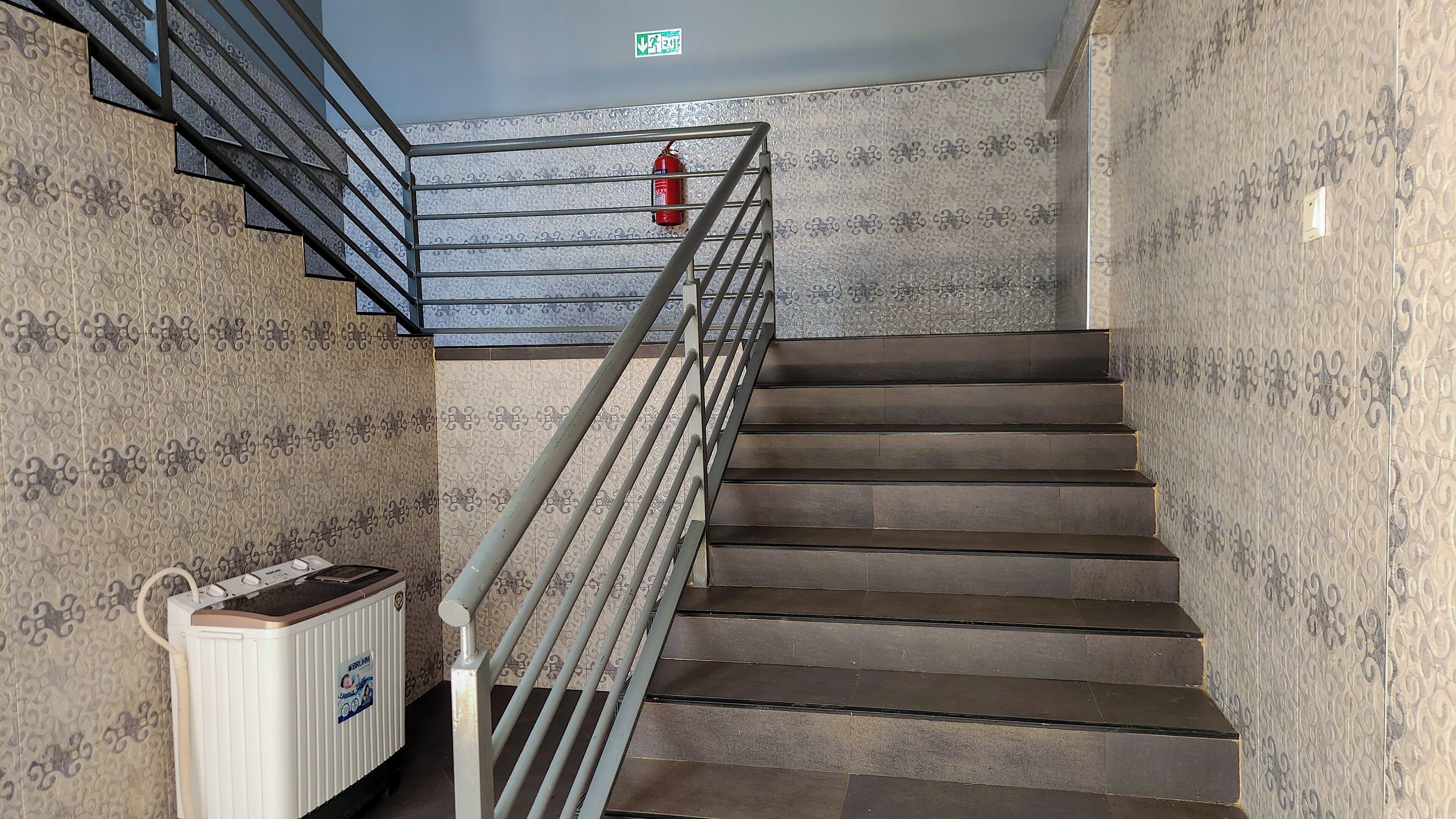 A staircase with a metal railing, patterned walls, and a fire extinguisher mounted on the wall.