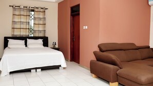 A bedroom with a bed, a nightstand, a lamp, a brown sofa, and a window with curtains. - GSM Crown Inn Hotel  (Ogbodjo)