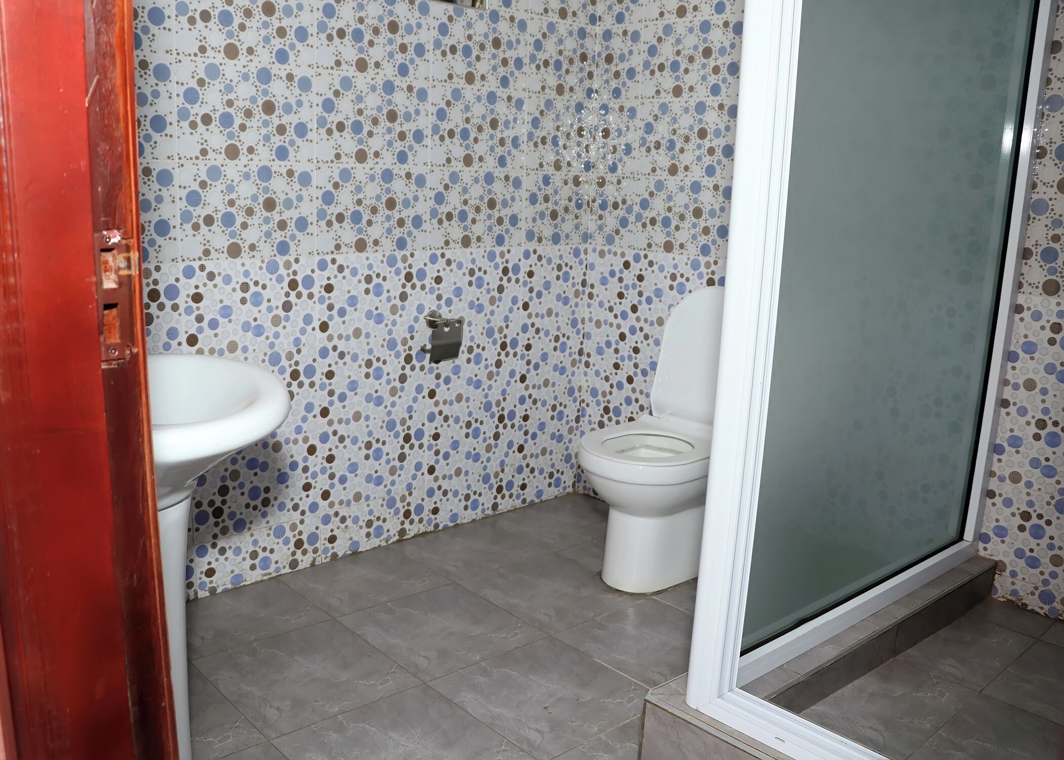 A bathroom with a white sink, toilet, and a shower area. The walls are tiled with a blue and brown polka dot pattern.