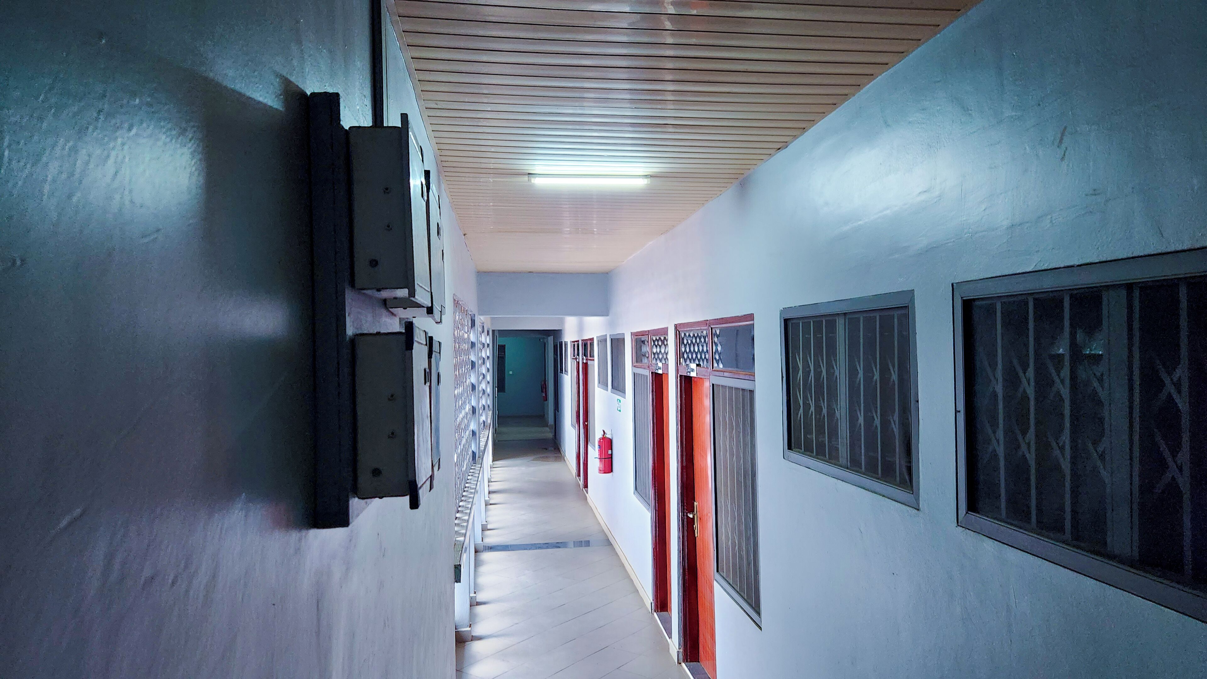 A corridor with doors and windows, a fire extinguisher, and a ceiling light.