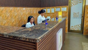 A reception desk with a marble top and wooden paneling, a glass partition, and framed certificates on the wall. - GSM Crown Inn Hotel  (Ogbodjo)