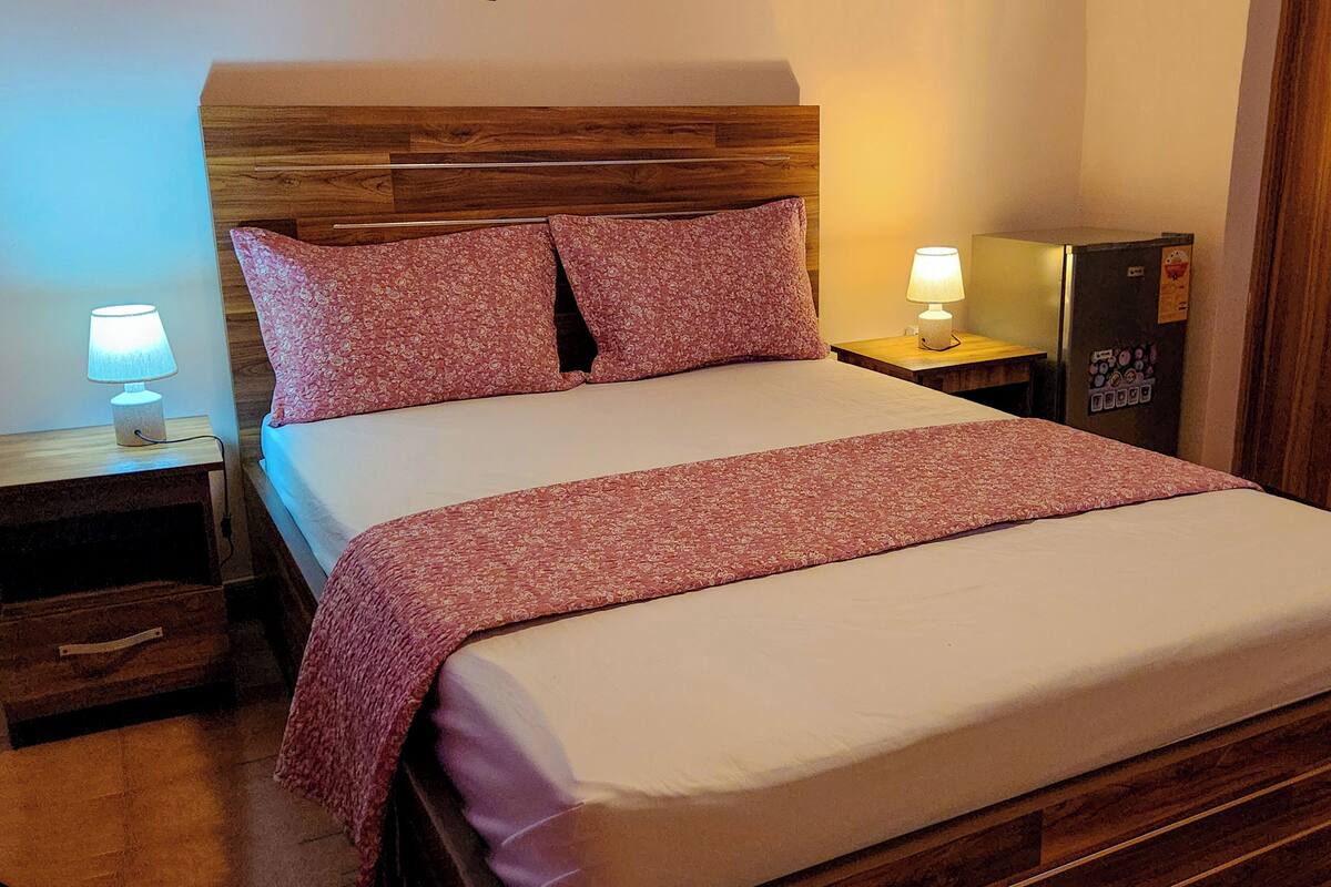 Una cama bien hecha con cabecera de madera, dos lámparas de noche y una mesita de noche pequeña de madera.
