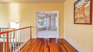 A hallway with wooden flooring leading to a bedroom with a bed and a ceiling fan.