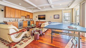 A spacious living area with a ping pong table, wooden cabinets, a sofa, and a large window.