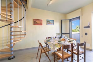 A dining area with a spiral staircase, a table set for six, and two paintings on the wall.