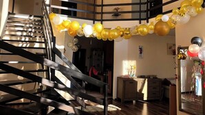 A staircase with a metal railing, a living area with a sofa and a coffee table, and a wall decorated with yellow and white balloons. - Pink Garden Events Advance Notice Required (Giarmata)