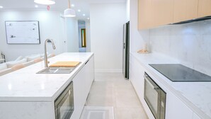 Une cuisine moderne avec des plans de travail en marbre blanc, des appareils électroménagers en acier inoxydable et des luminaires suspendus.