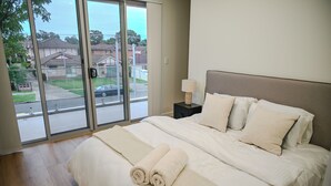 Une chambre avec un grand lit, une table de chevet et une vue sur l’extérieur, accessible par une porte-fenêtre coulissante.