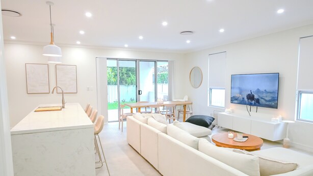 Un salon moderne avec un canapé blanc, une table basse en bois et un téléviseur fixé au mur.