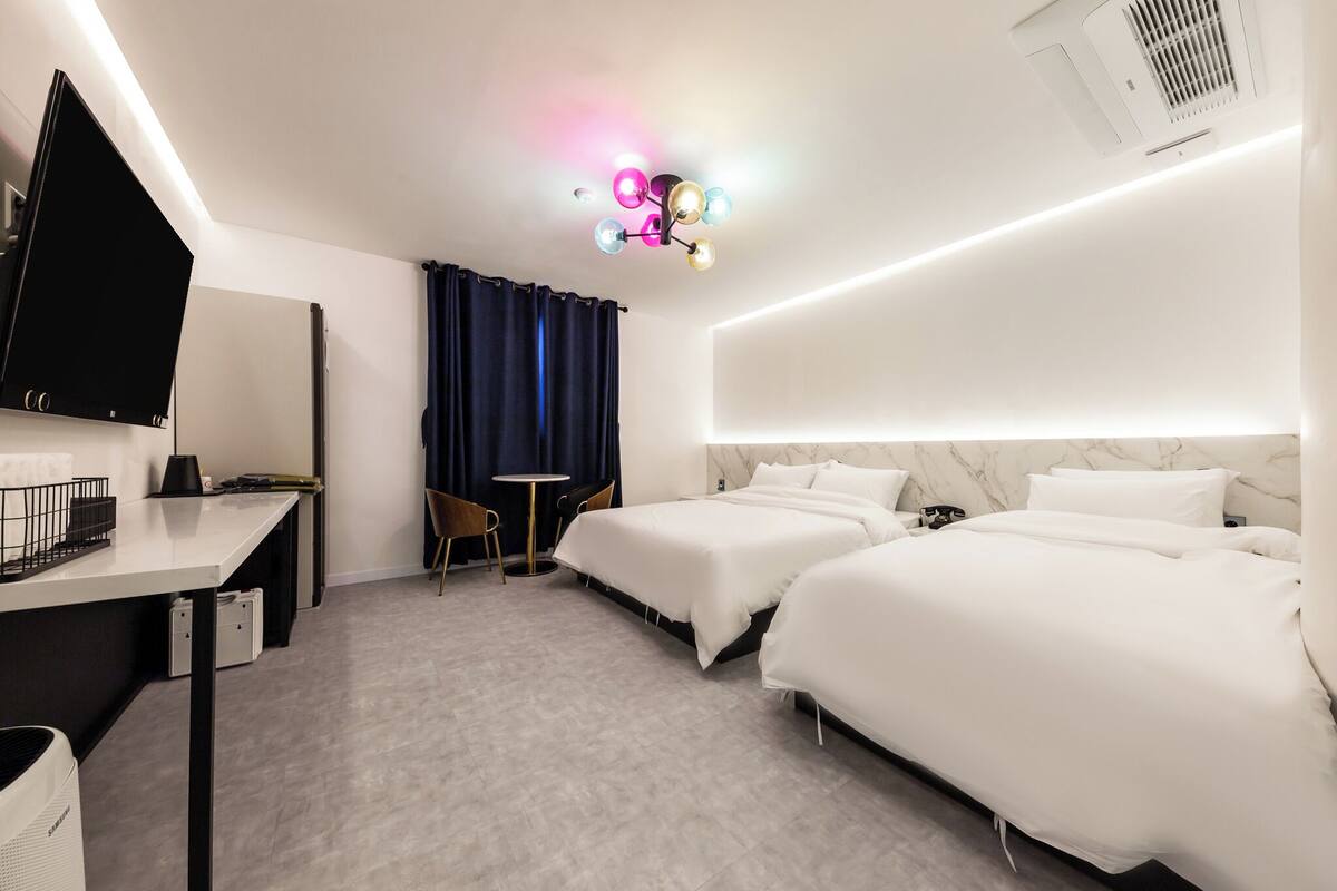 Habitación de hotel con dos camas, un escritorio, una silla, un televisor y una lámpara en el techo.