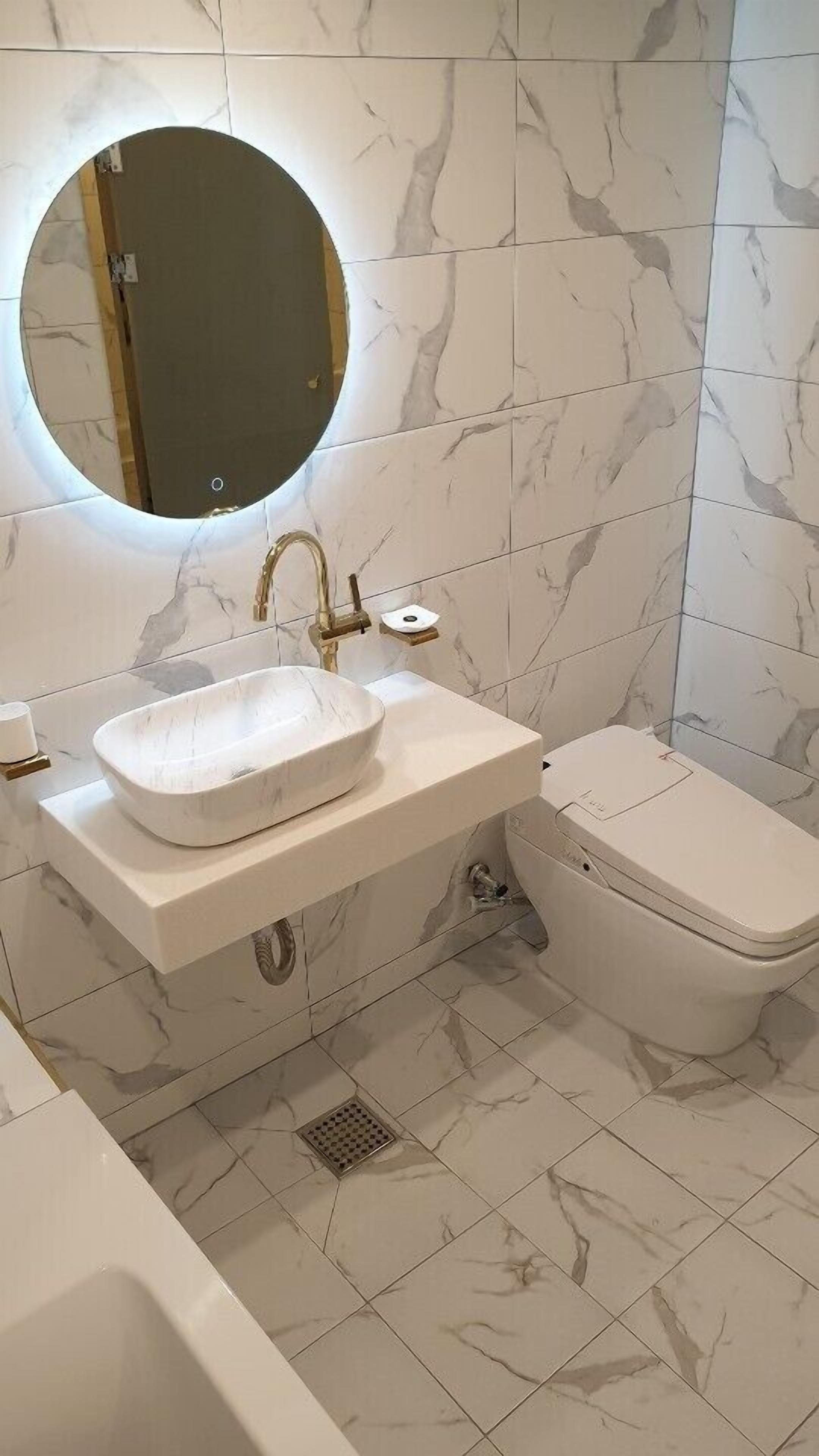 A bathroom with a white marble sink, a round mirror, and a toilet.
