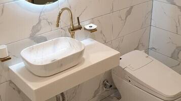 A bathroom with a white marble sink, a round mirror, and a toilet.
