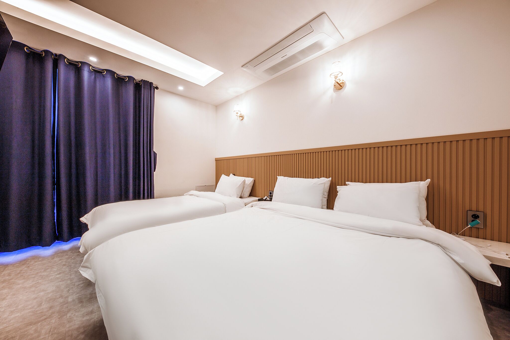 A hotel room with a large bed, a wooden headboard, a bedside table, and an air conditioning unit.