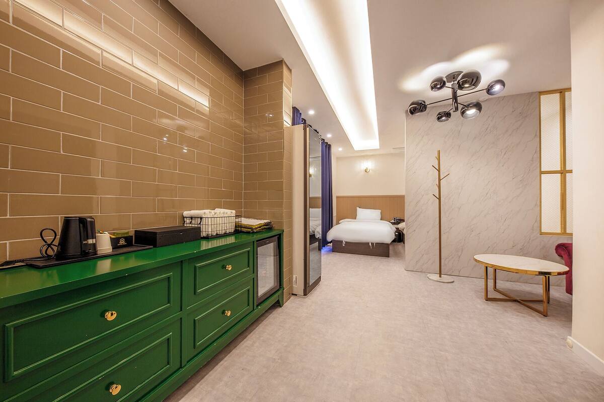 Habitación de hotel moderna con tocador verde, pared de mármol, cama y una mesita.