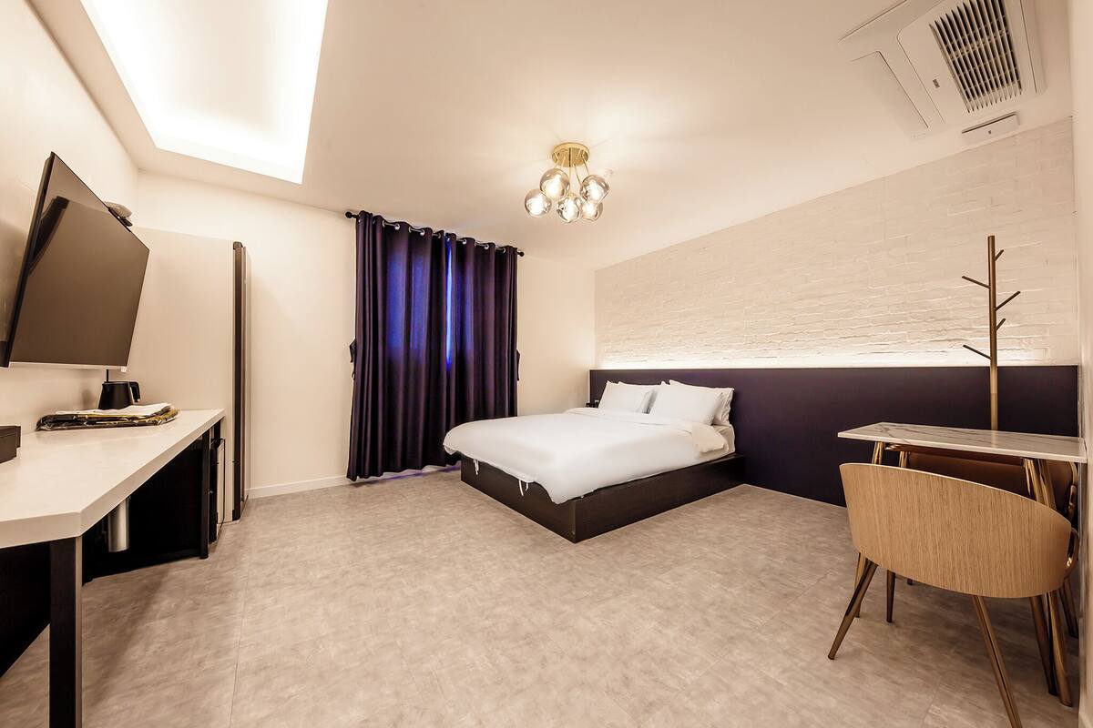 Habitación de hotel moderna con cama, escritorio, silla y televisor de pantalla plana.
