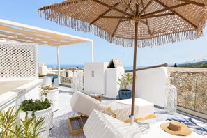 A rooftop terrace with white furniture, a woven umbrella, and potted plants. - Roof Garden-Panoramic View and Jacuzzi (Rethymno)