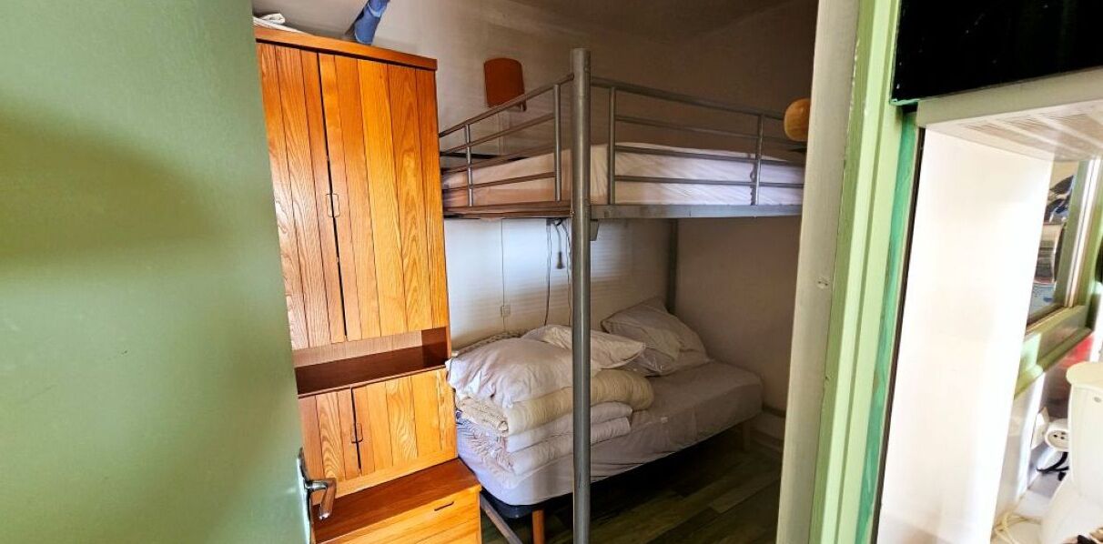 Dormitorio con literas, un armario de madera y una escalera de metal.