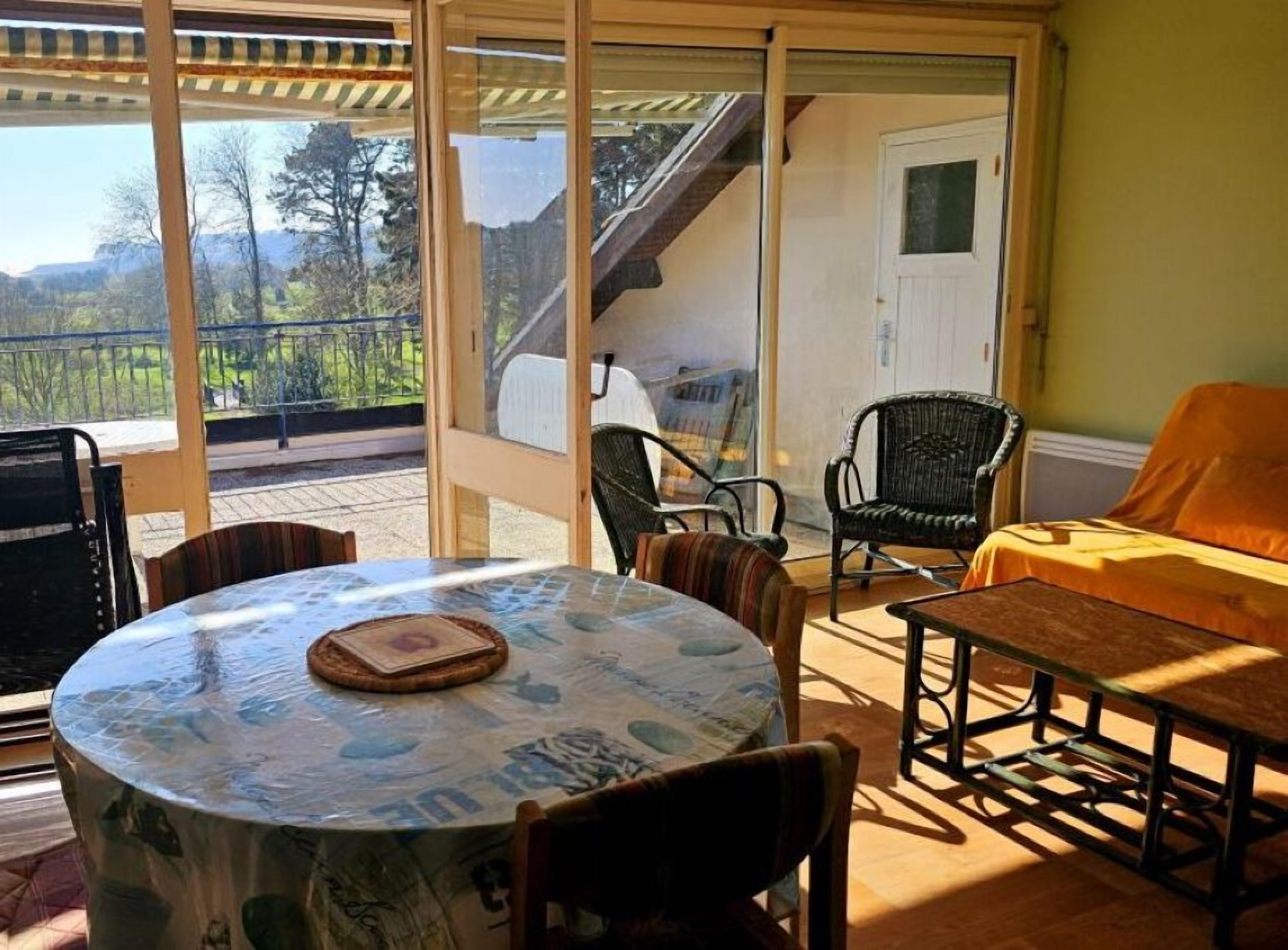 Ein gemütlicher Patio-Bereich mit einem runden Tisch, Stühlen und einer Bank. Eine Treppe führt zu einer oberen Ebene mit einer Tür.
