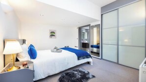Ein modernes Hotelzimmer mit einem Bett, einem Schreibtisch mit Lampe, einem kleinen Tisch mit Kerze und einer großen Schiebetür aus Glas, die auf einen Balkon führt.