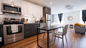 Una cocina moderna con electrodomésticos de acero inoxidable, un comedor con mesa y sillas, y una sala de estar con sofá y ventana.
