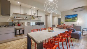 A modern kitchen with a dining area, featuring a large island, bright orange chairs, and a unique spherical light fixture. - Lucy Florence Charming Modern Apartment  (Florence)