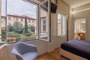 A bedroom with a large window, a chair, a bed, and a bathroom visible through an open door. - Lucy Florence Charming Modern Apartment  (Florence)