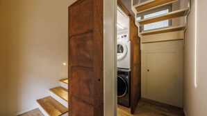 A laundry room with a washing machine and dryer, wooden steps leading to a door, and a staircase with wooden railings. - Lucy Florence Charming Modern Apartment  (Florence)