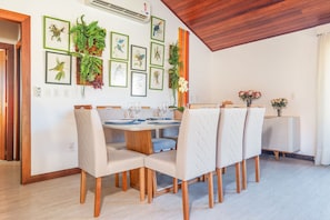 A dining area with a round table, six chairs, and framed botanical prints on the wall. - Bz78 Centro Cobertura com 2 suítes e SPA (Buzios)