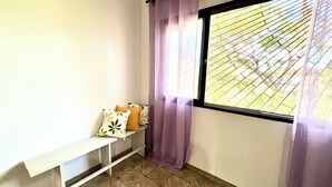 Ein Eckzimmer mit einer Sitzbank, einem Fenster mit Blick auf Grünflächen und einem violetten Vorhang.