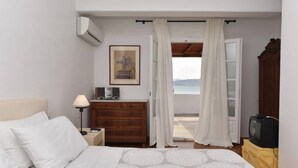 Une chambre à coucher comprenant un lit, une table de chevet, une commode, un téléviseur et une vue sur la mer, visible par une porte ouverte.