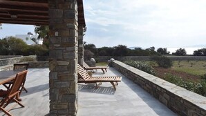 Une terrasse extérieure avec des piliers en pierre, des fauteuils de jardin en bois et une table.