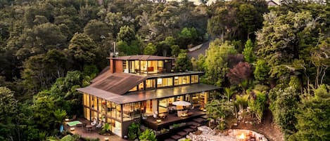 Una casa moderna de dos pisos con fachada de vidrio, rodeada de un bosque denso.