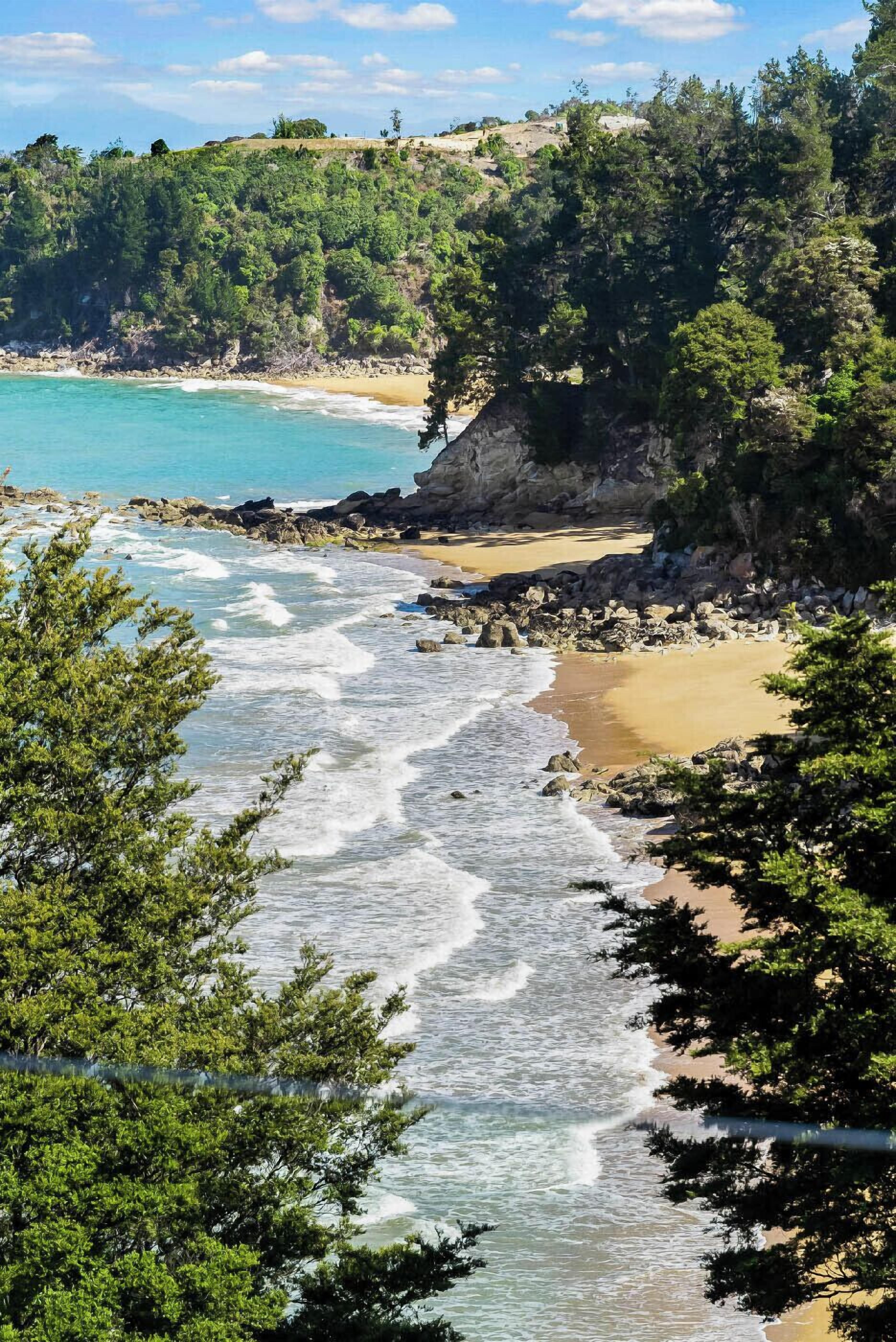 A coastal landscape with a beach, rocky shoreline, and dense greenery.