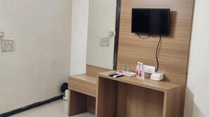 Une petite chambre moderne, dotée d’un bureau en bois, d’un téléviseur à écran plat fixé au mur et d’une petite étagère sur laquelle sont posés quelques objets.