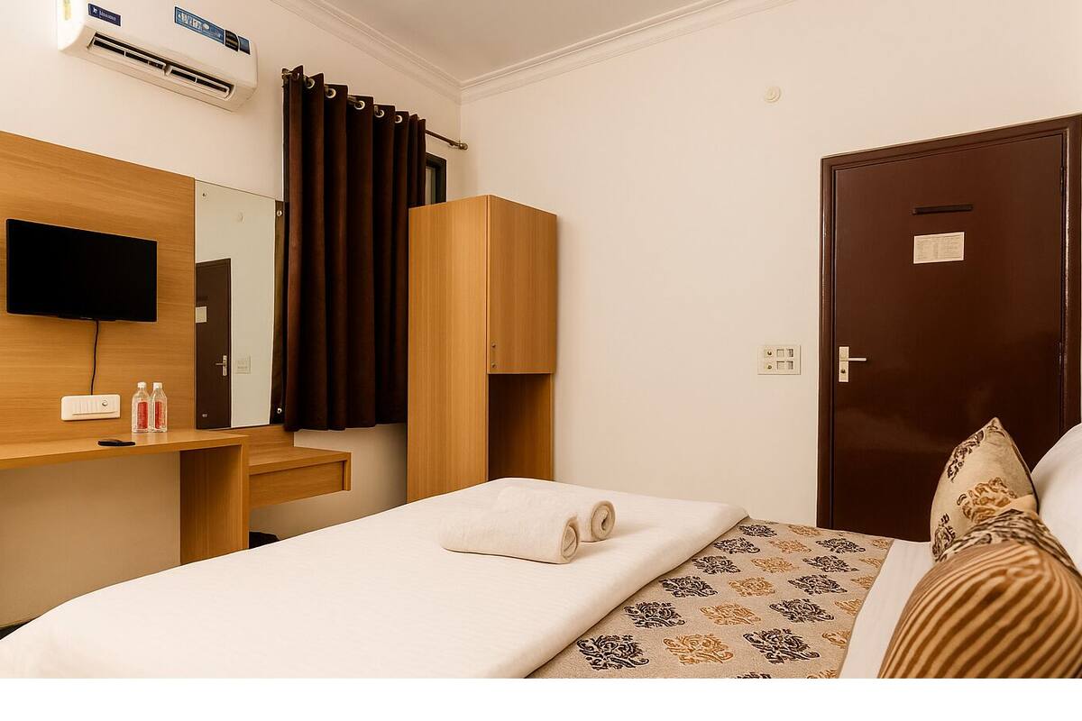 Habitación de hotel con cama, escritorio, televisor de pantalla plana, armario, puerta y espejo.