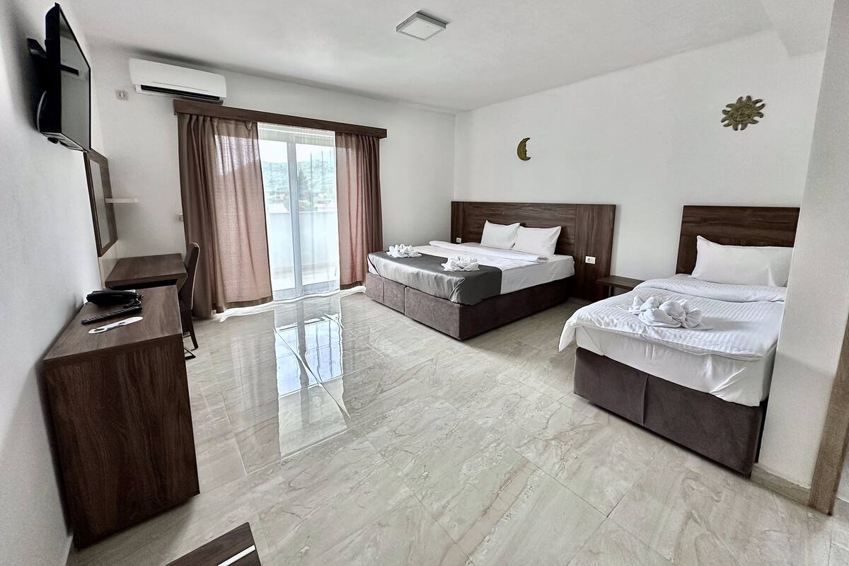 A hotel room with a bed, a desk, a chair, a TV, and a window with curtains.