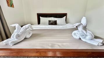 A neatly made bed with white towels arranged in a decorative pattern, a wooden headboard, and a dark leather ottoman.