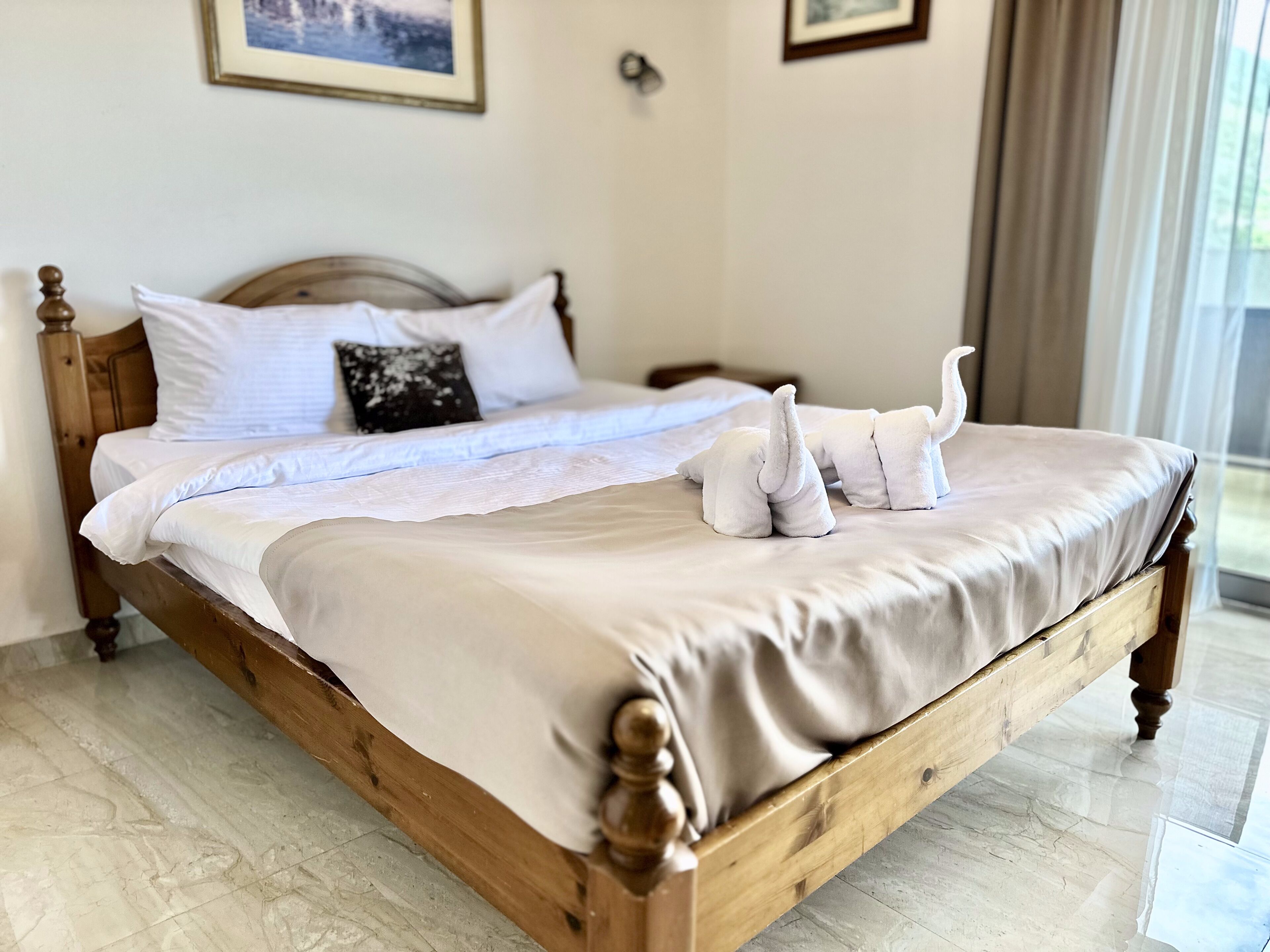 A wooden bed with white linens and two elephant-shaped towels.