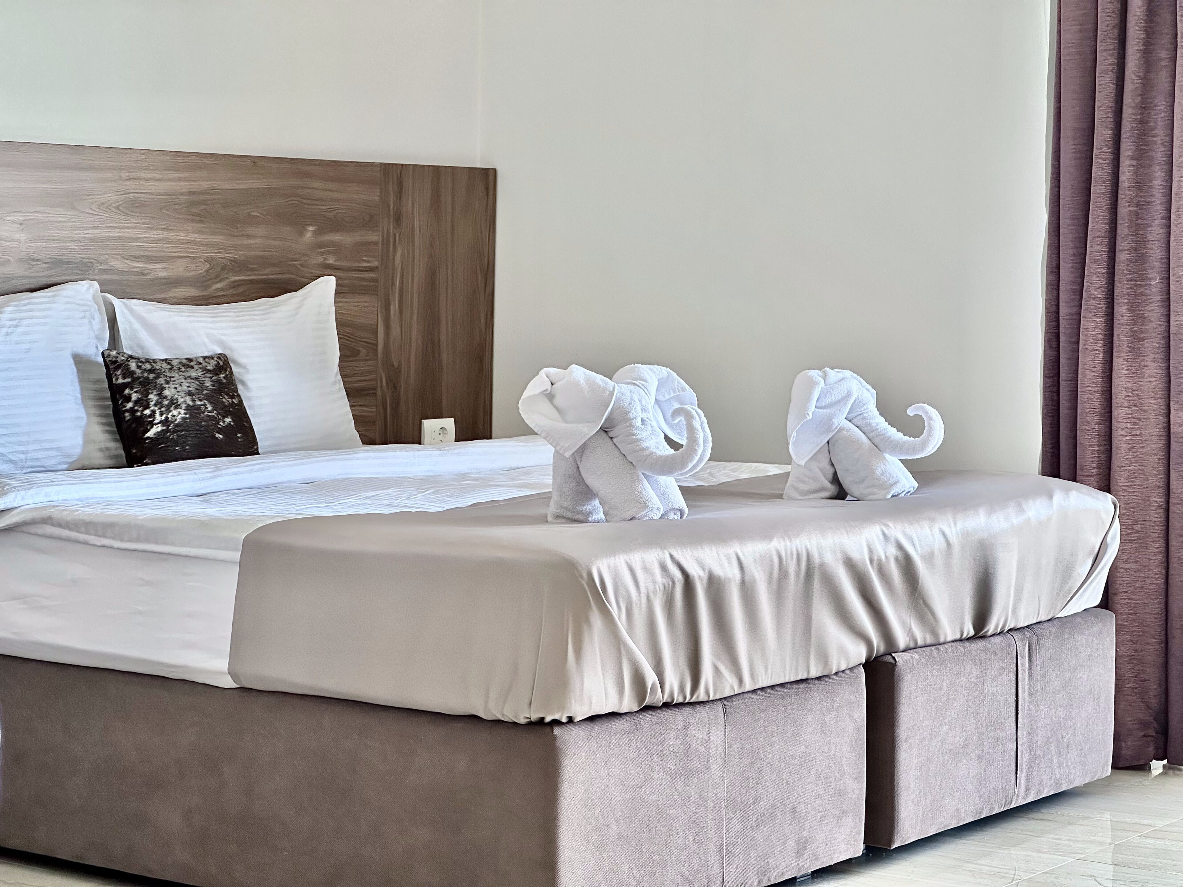 A neatly made bed with a wooden headboard, two pillows, and two towels shaped like elephants.