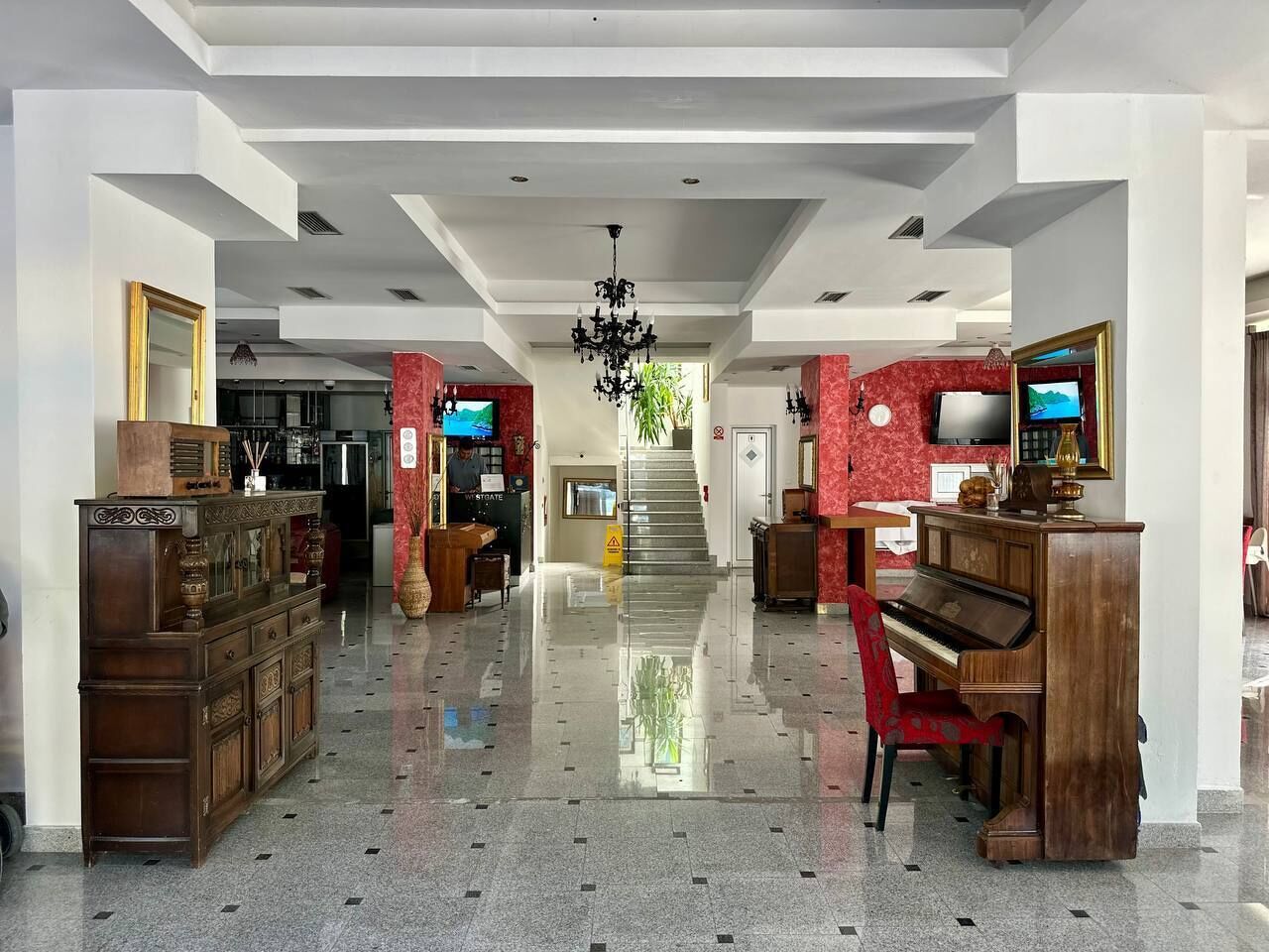 Un hall de hotel con un piano de cola, una mesa de recepción y una escalera que conduce a los pisos superiores.