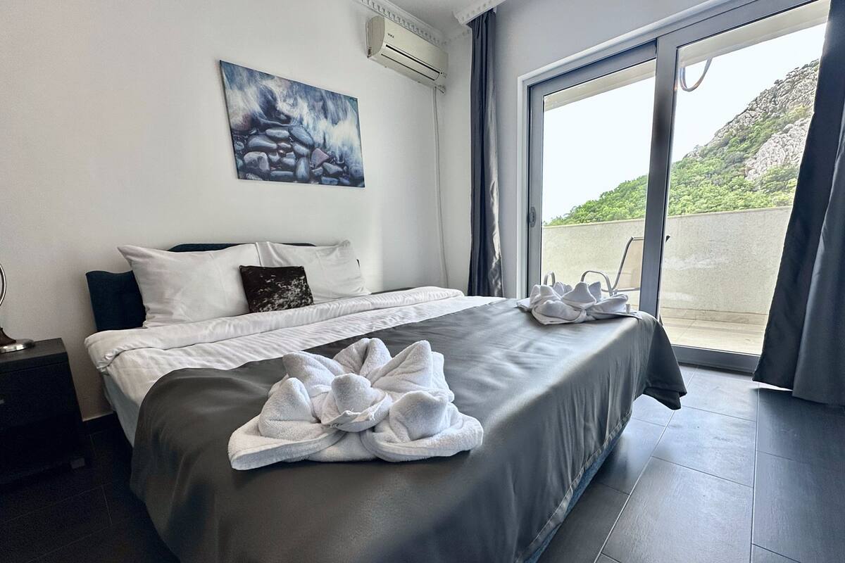 A modern hotel room with a large bed, a painting on the wall, and a view through the glass door.