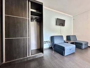 A modern room with a built-in closet, a flat-screen TV mounted on the wall, and two grey sofas. - West Gate (Sutomore)